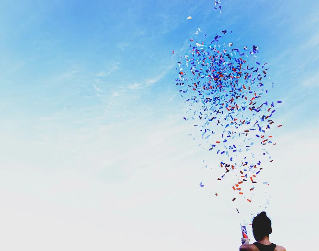 Person launching a burst of red, white, and blue confetti into a bright blue sky in celebration