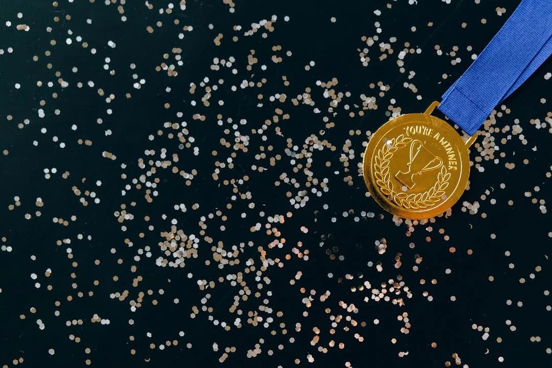 Gold winner's medal on a blue ribbon lying on a dark surface scattered with confetti
