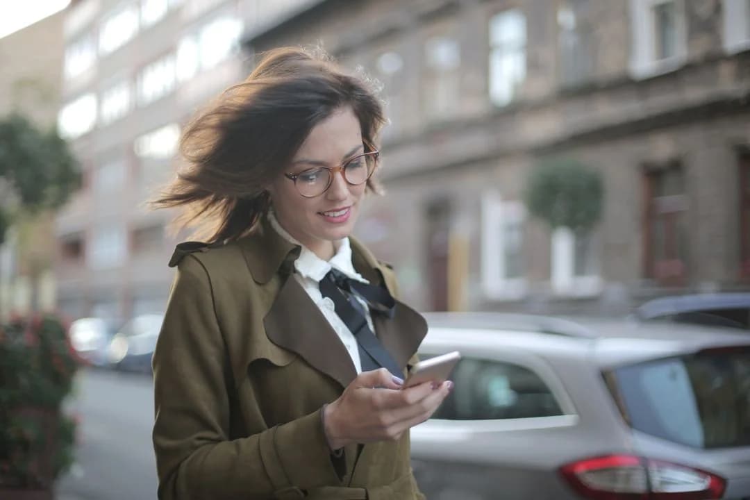 Woman in glasses answering a survey on her phone while walking down a city street, capturing life in the moment