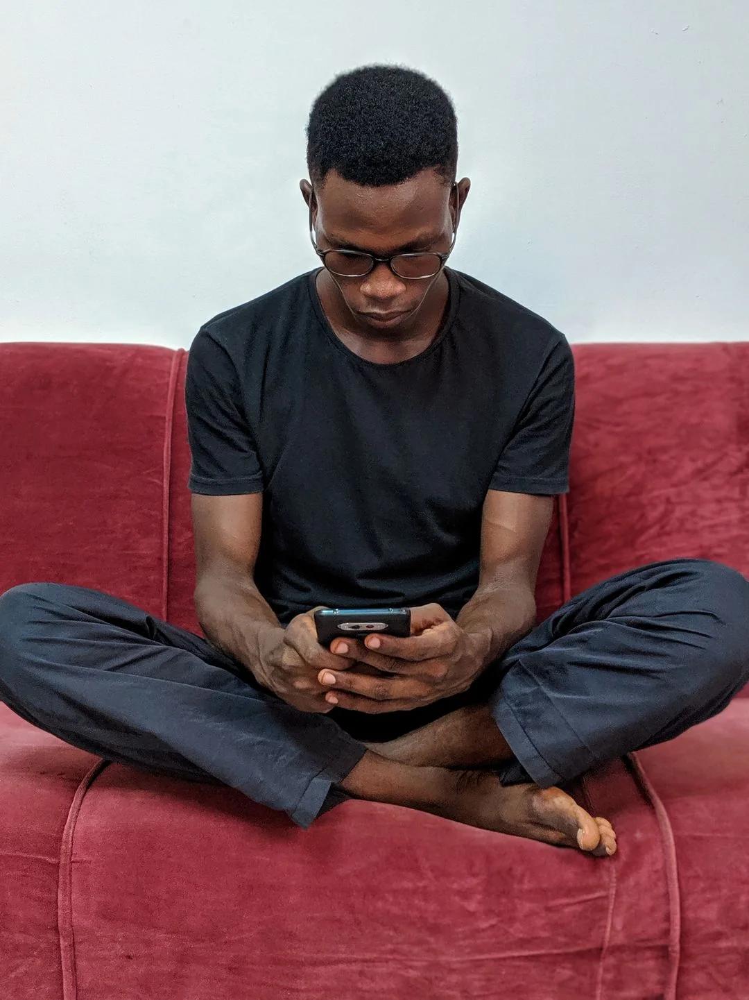 Young man with glasses sitting cross-legged on a red couch, reading an intervention prompt on his smartphone