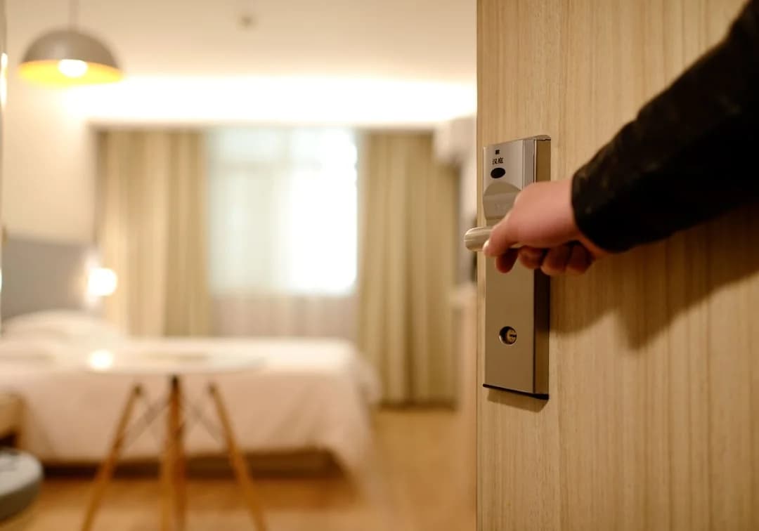 Hotel worker's hand on the door handle of a bright, freshly made-up guest room