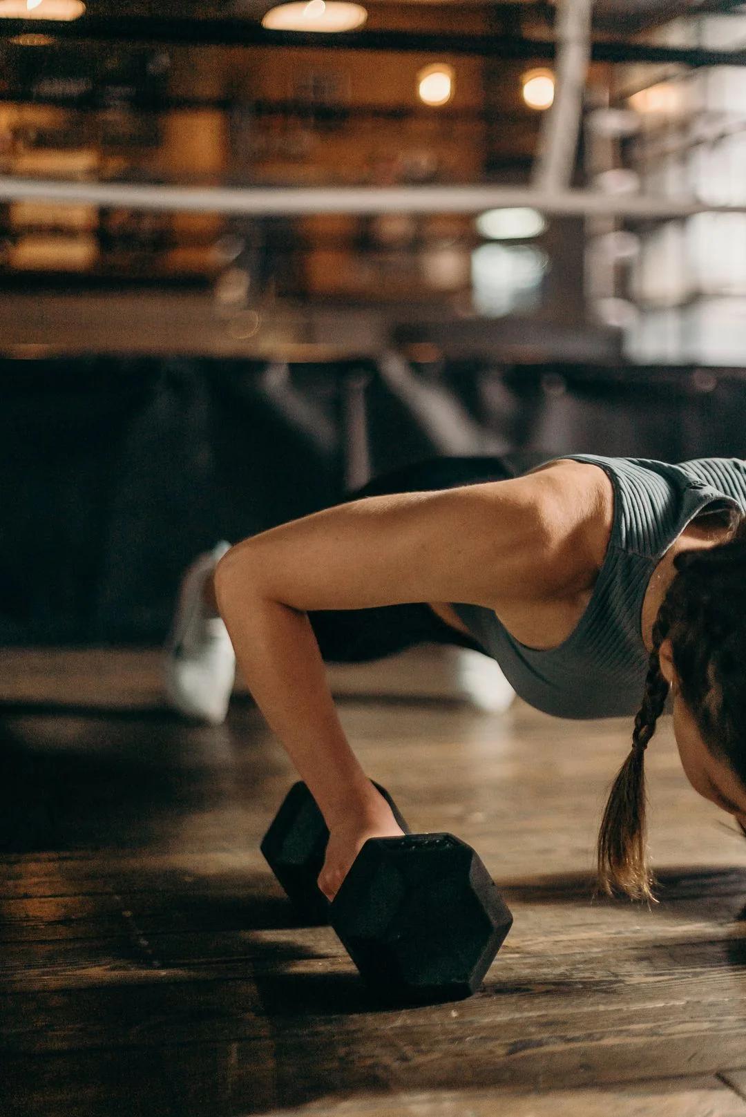 Athlete doing push-ups on dumbbells on a gym floor beside a boxing ring during training