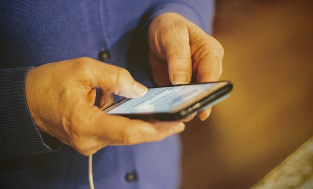 Close-up of an older adult's hands filling out a survey form on a smartphone