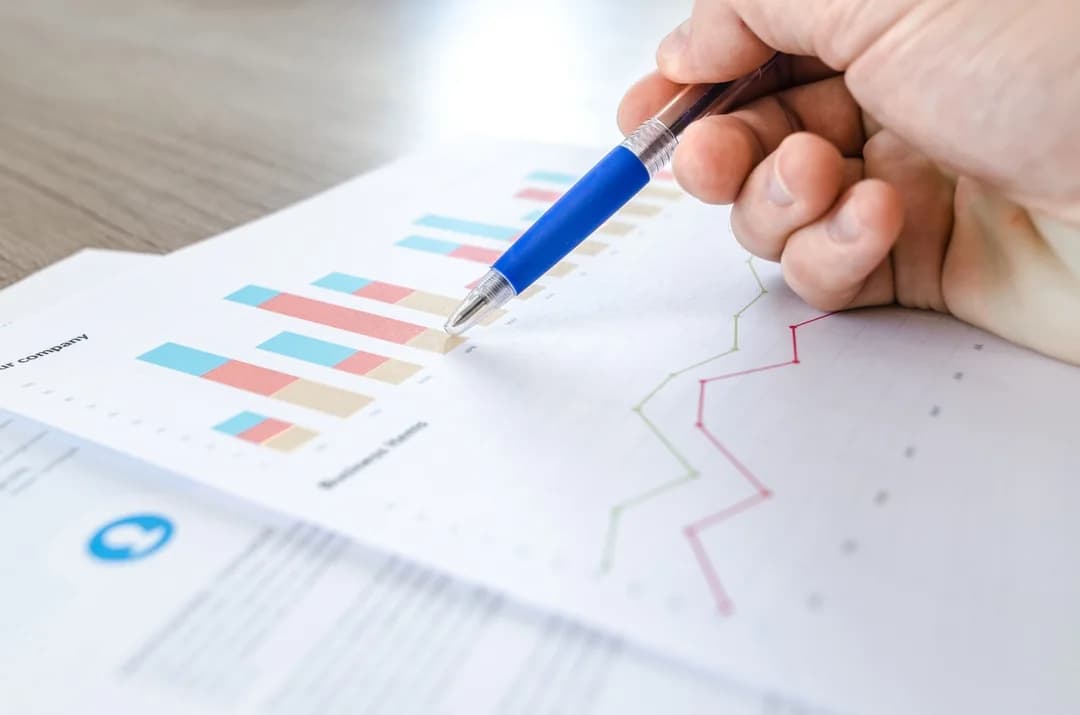 Hand holding a blue pen over printed bar and line charts while reviewing study data on paper reports