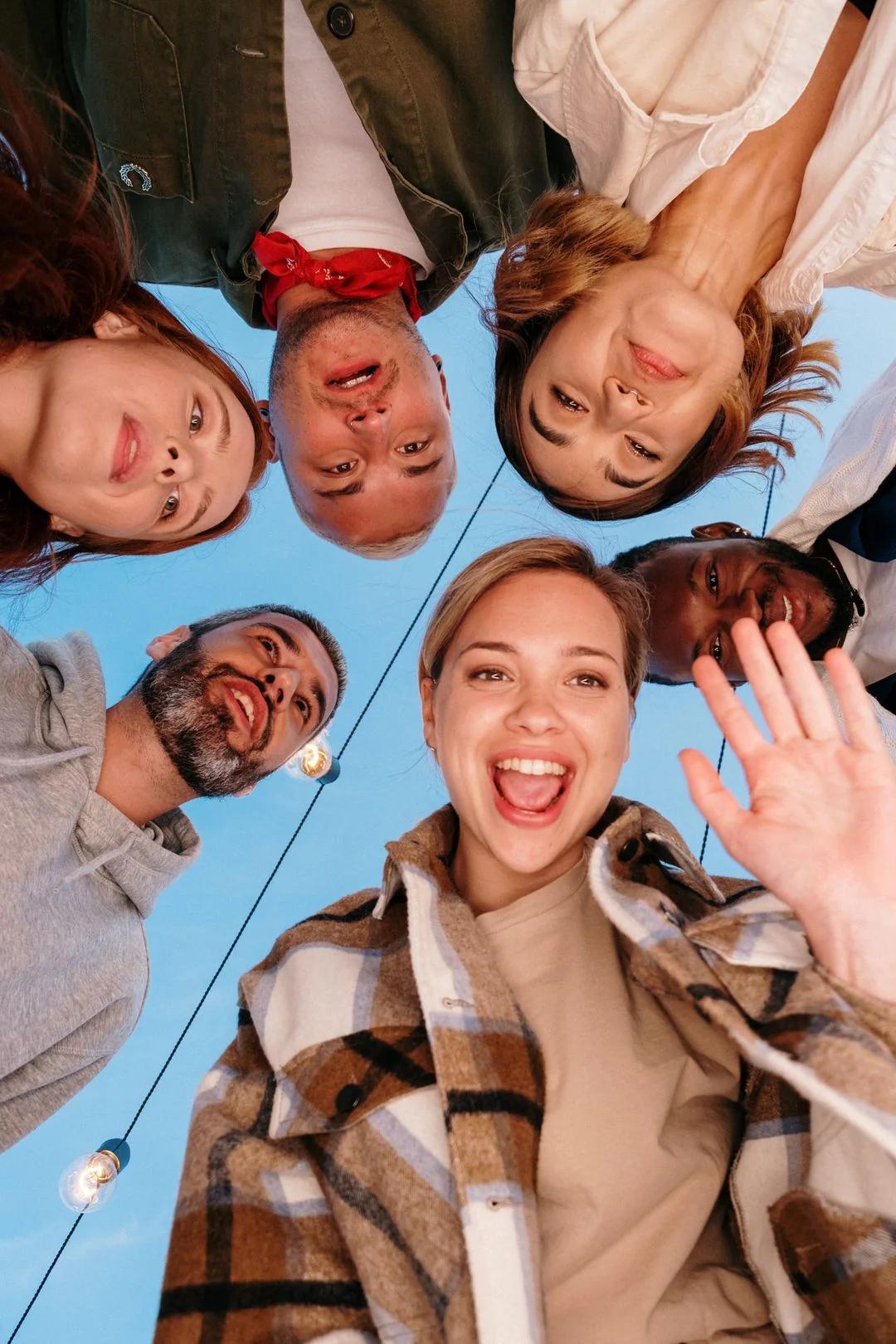Diverse group of smiling coworkers huddled in a circle, photographed from below against a blue sky