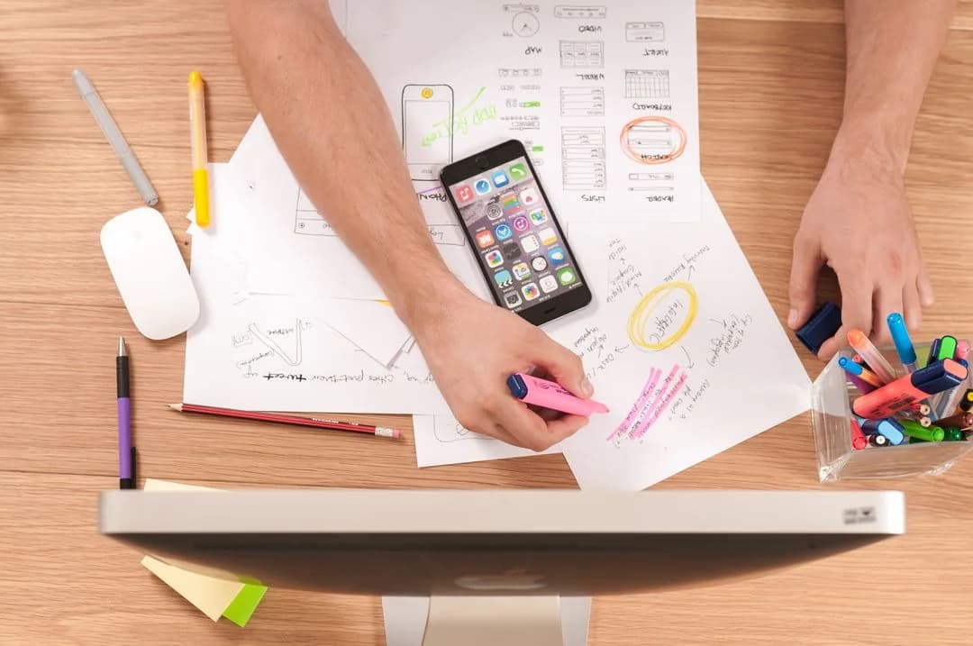 Designer highlighting app wireframe sketches around a smartphone on a desk, planning a mobile research app