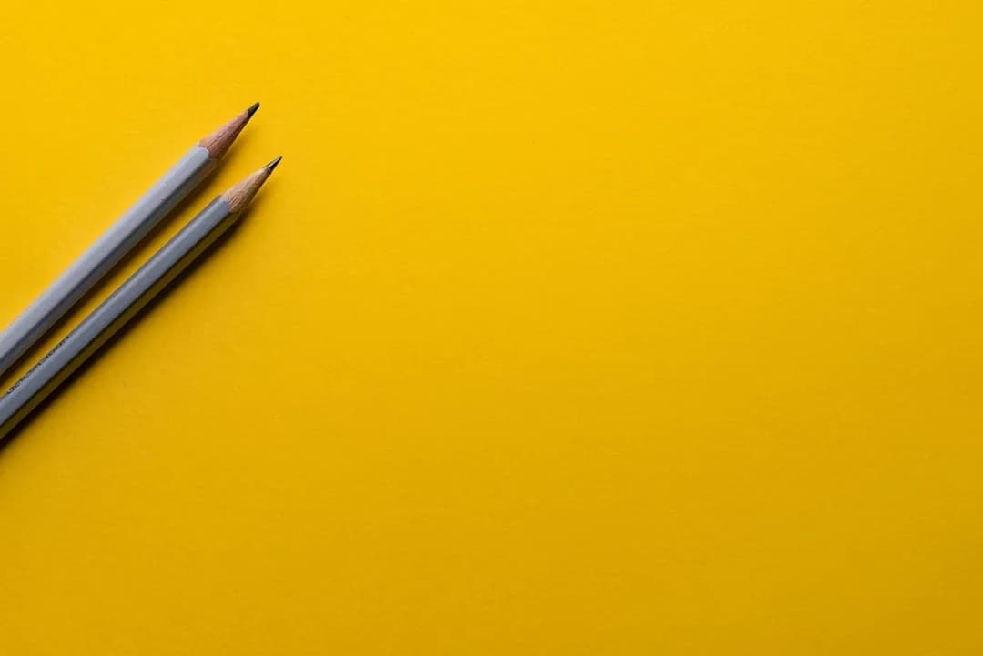Two sharpened grey pencils lying diagonally on a bright yellow background, evoking dissertation writing