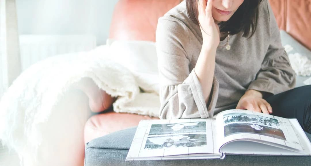 Woman on a couch leafing through a photo album, recalling autobiographical memories