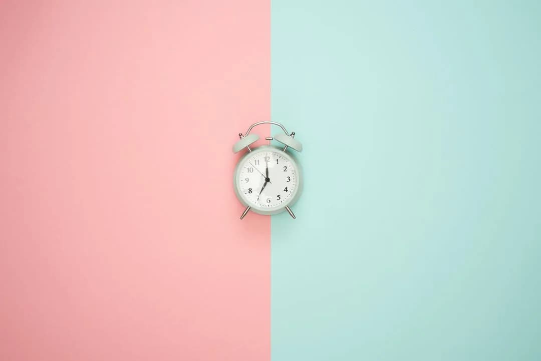 Vintage alarm clock centered on a split pastel pink and mint background, symbolizing just-in-time intervention timing