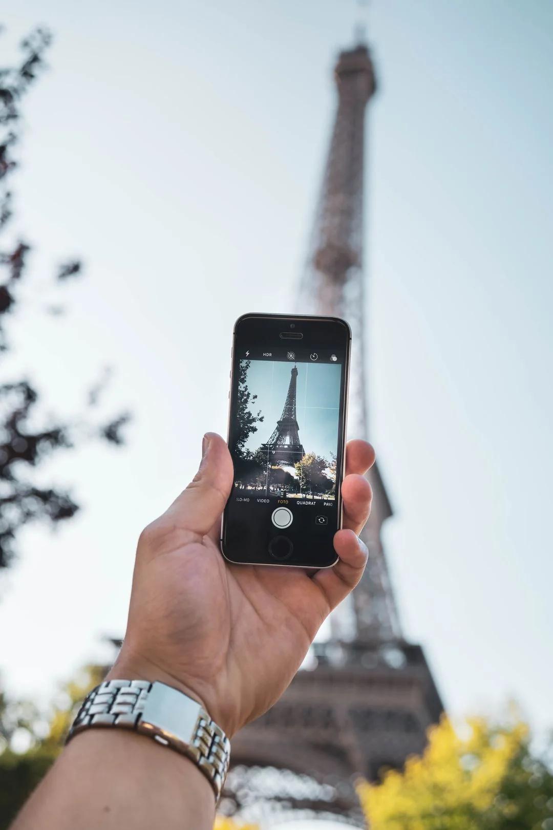 Main tenant un smartphone qui photographie la tour Eiffel, symbole de la recherche EMA francophone
