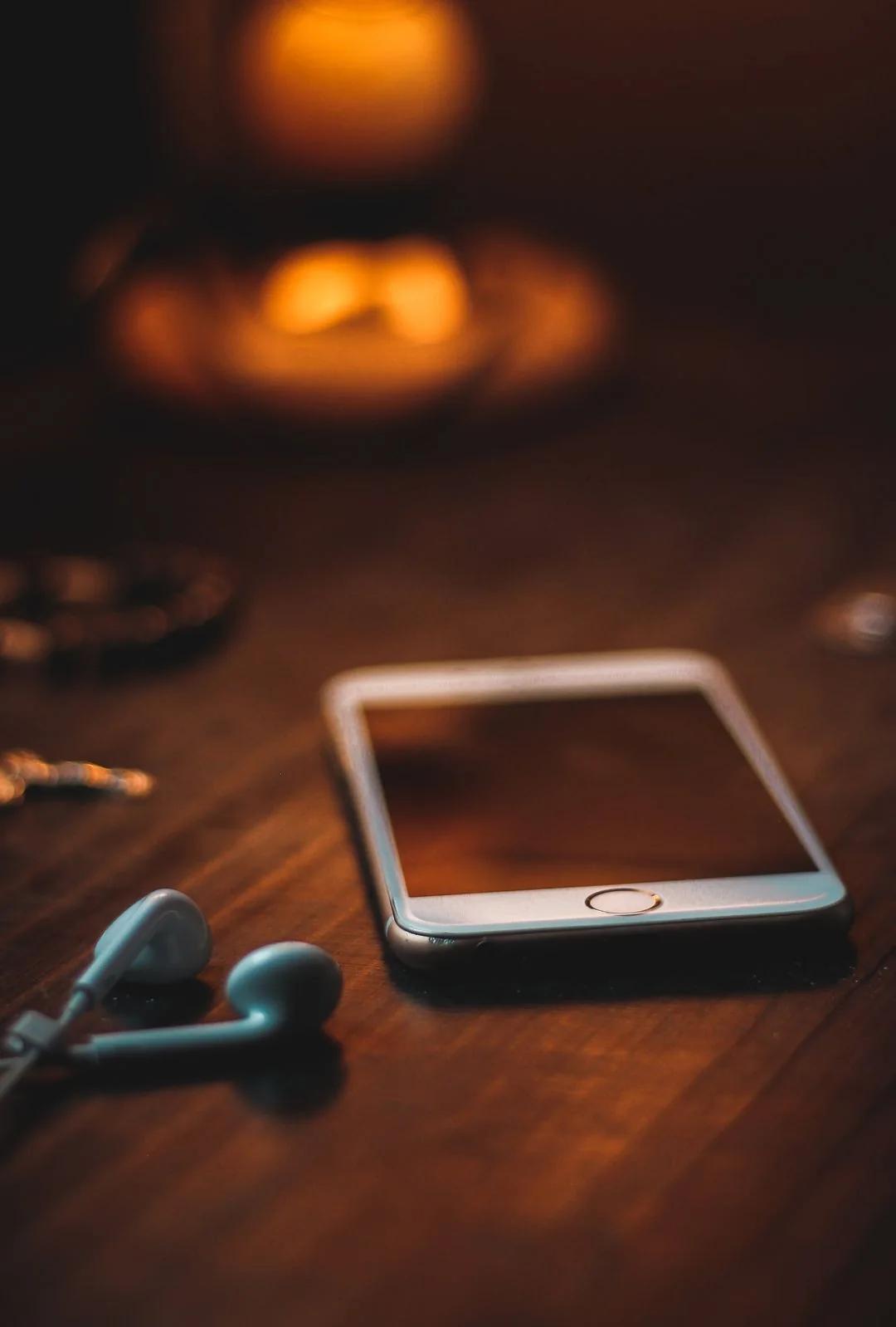 Smartphone and earbuds resting on a wooden table in warm candlelight, hinting at everyday moments captured by ESM