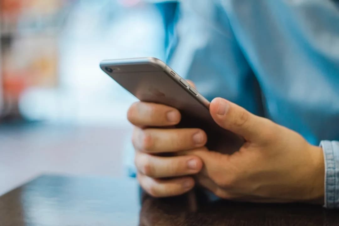 Close-up of hands holding a smartphone at a table, answering an in-the-moment experience sampling prompt