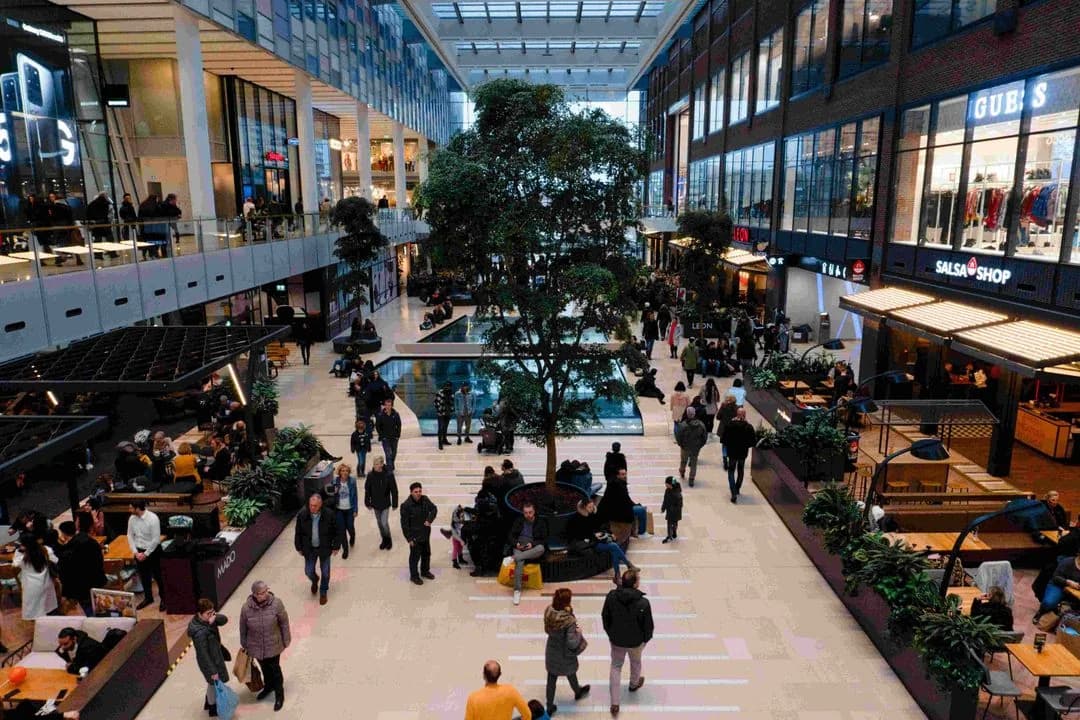 Shoppers strolling through a bright multi-level shopping mall lined with stores and cafes